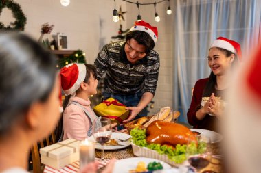 Asyalı aile Noel partisinde küçük kızına hediye paketi veriyor. Çekici küçük kız, yemek yerken akrabalarından hediyeler alır Şükran Günü 'nü birlikte yemek masasında kutlarız.