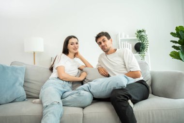 Kafkasyalı genç bir çiftin portresi oturma odasında kanepede oturur. Çekici romantik yeni evli erkek ve kadın gülümseyen ve kameraya bakan evde sevgililer gününde birlikte vakit geçirmenin tadını çıkarın..