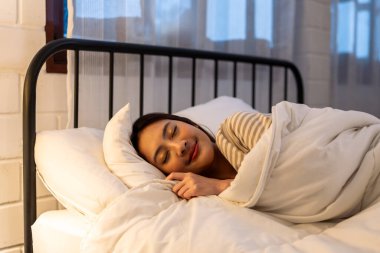 Asian beautiful woman lying down on bed in bedroom, dreaming at night. Attractive young female in pajamas sleeping alone on comfortable pillow and cozy blanket in dark room for health care at home.