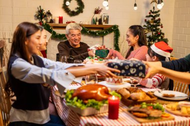 Asyalı sevimli aile evde Noel partisinde hediyelerini değiş tokuş ediyor. Bir grup çekici insan yemek masasında bayram kutlaması yaparken birbirlerinden hediye paketi alıyorlar.