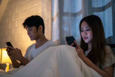 Asyalı genç telefon bağımlısı çift birbirlerine dikkat etmezler. Aile sorunu, yeni evli erkek ve kadın partner yatakta oturuyor, akıllı telefon kullanıyor, yatak odasında karı ve kocayı görmezden geliyor..