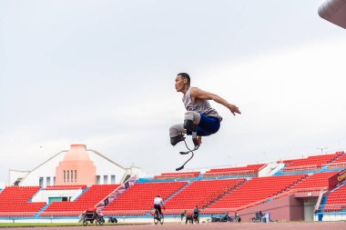 Protez bıçaklı Asyalı sporcu stadyumda vücut ısıtıyor. Çekici ampüte sporcu koşucusu yaklaşan Paralimpik koşu yarışması için egzersiz oturumundan önce kendini hazırla