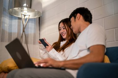 Asyalı genç adam geceleri karısıyla birlikte cep telefonu kullanıyor. Pijamalı çekici bir eş kocasını bekliyor dizüstü bilgisayarını kullanıyor yatmadan önce internette iletişim kuruyor..