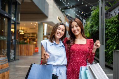 Alışveriş merkezindeki Asyalı kadınların portresi. Çekici iki kız alışveriş torbaları tutarken kameraya bak ve mutlulukla yürürken alışveriş merkezinden alışveriş yap..
