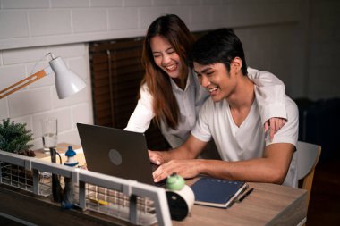 Asyalı genç adam gece evde karısıyla birlikte yatak odasında çok çalışıyor. Pijamalı çekici bir eş kocasını bekliyor dizüstü bilgisayarını kullanıyor yatmadan önce internette iletişim kuruyor..