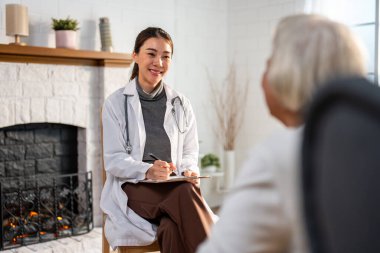 Asyalı genç bakıcı hemşireyi muayene et ve yaşlı kadın hastayı dinle. Çekici uzman bakıcı kadınlar, evdeki yaşlı olgun büyükannelere danışmanlık ve danışmanlık yaparlar..