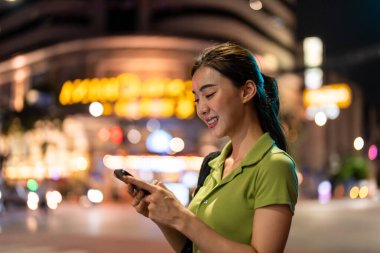 Asyalı çekici kadın gezgin şehirde yürürken telefonla konuşuyor. Güzel kadın turist gezgin akıllı telefon kullanarak tek başına seyahat ediyor. Tatilde gece yollarında iyi vakit geçiriyor..