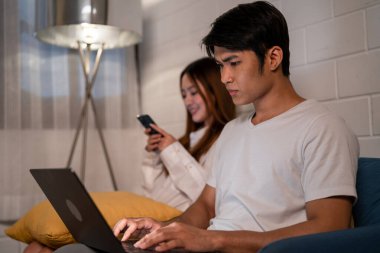 Asyalı genç adam geceleri karısıyla birlikte dizüstü bilgisayarda çalışıyor. Pijamalı çekici bir kız arkadaş akıllı telefon kullanıyor. Bekleyen koca evde yatmadan önce bilgisayarla iletişim kuruyor.