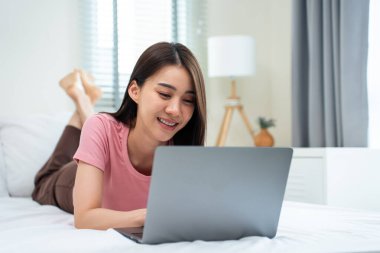 Asyalı çekici kadın sabahları evde dizüstü bilgisayar sohbeti yapıyor. Mutlu, sıradan, güzel bir kadın yatak odasında uzanıyor. Tatil haftasonunun keyfini çıkarın. Evdeki teknolojiyle çevrimiçi laptop iletişimini kullanın.