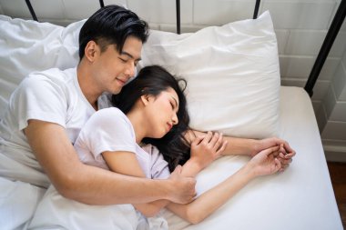 Asyalı çekici bir adam yatakta uzanırken kız arkadaşına sarılıyor. Çekici, yeni evli çift pijamalarıyla sabah erken saatlerde yatak odasında eğleniyor. Aile ilişkisi kavramı