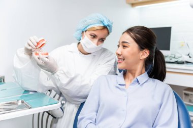 Beyaz dişçi diş sağlığı kliniğindeki genç kız için dişleri muayene ediyor. Diş hekimliği koltuğunda yatan çekici kadın hastanede muayene sırasında doktordan diş tedavisi görüyor.