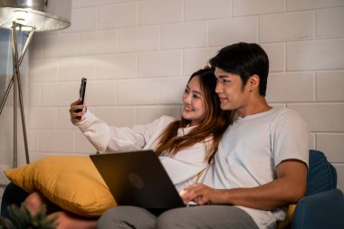 Asyalı genç adam gece telefonda karısıyla birlikte çalışıyor. Pijamalı çekici bir eş kocasını bekliyor dizüstü bilgisayarını kullanıyor yatmadan önce internette iletişim kuruyor..