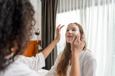 Yatak odasında yüz maskesi takan iki güzel kadın. Yatakta oturan çekici bayan arkadaşlar, duş üstüne krem sürerler güzellik tedavisi için nazikçe kaplıcaya giderler.