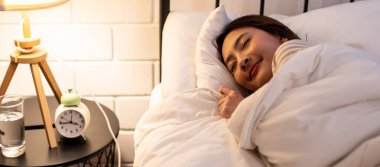Asian beautiful woman lying down on bed in bedroom, dreaming at night. Attractive young female in pajamas sleeping alone on comfortable pillow and cozy blanket in dark room for health care at home.
