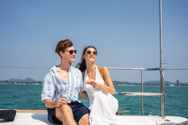 Kafkasyalı romantik çift yat gezisi sırasında güzel manzaraya bakıyor. Çekici bir genç adam ve kadın birlikte takılıp yıl dönümü balayı gezisini kutlarken katamaran teknesi yaz günbatımında yelken açıyor.