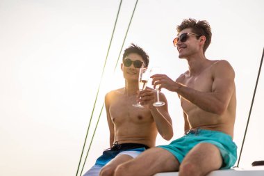 Beyaz erkek arkadaş yatta parti yaparken şampanya içiyor. Birlikte takılan yakışıklı erkek turist yaz günbatımında katamaran teknesiyle açılırken tatil tatilini kutluyor..