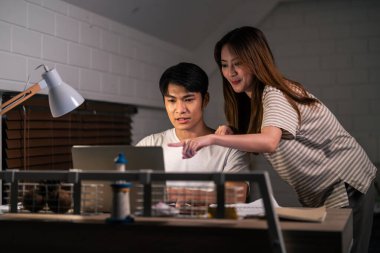 Asyalı genç adam gece evde karısıyla birlikte yatak odasında çok çalışıyor. Pijamalı çekici bir eş kocasını bekliyor dizüstü bilgisayarını kullanıyor yatmadan önce internette iletişim kuruyor..