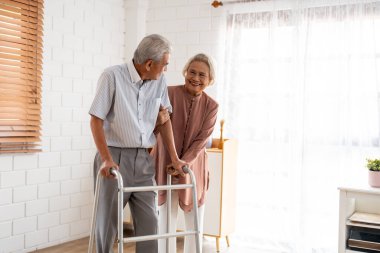 Asyalı çekici yaşlı kadın, Walker 'la yürüyen yaşlı adamı destekliyor. Mutlu bir aile, güzel olgun bir çift emeklilikten sonra evde birlikte oturma odasında fizik tedavi yapıyorlar..