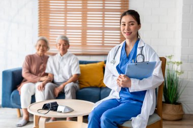 Asyalı güzel bakıcının portresi. Evdeki yaşlı çifte iyi bak. Çekici uzman bakıcı kadınlar huzurevinde yaşlı ve olgun büyükbabalarına destek oluyor ve kameraya bakıp gülümsüyorlar..