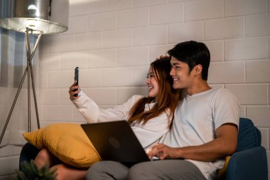 Asyalı genç adam gece telefonda karısıyla birlikte çalışıyor. Pijamalı çekici bir eş kocasını bekliyor dizüstü bilgisayarını kullanıyor yatmadan önce internette iletişim kuruyor..