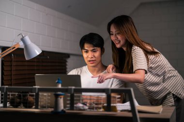 Asyalı genç adam gece evde karısıyla birlikte yatak odasında çok çalışıyor. Pijamalı çekici bir eş kocasını bekliyor dizüstü bilgisayarını kullanıyor yatmadan önce internette iletişim kuruyor..