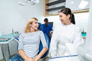 Kadın diş hekimi, diş sağlığı kliniğindeki beyaz dişli kızı muayene ediyor. Diş hekimliği koltuğunda yatan çekici kadın hastanede muayene sırasında doktordan diş tedavisi görüyor.