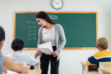 Bir grup öğrenci ilkokulda sınıfta öğretmenle birlikte öğreniyor. Çekici, güzel bayan eğitmen. Anaokulunda küçük çocukları mutluluk ve eğlence ile eğitmek ve eğitmek..