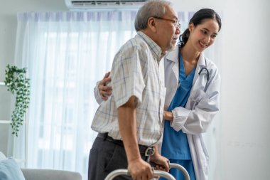 Asyalı yaşlı adam bakıcı ile fizik tedavi yapıyor. Çekici uzman bakıcı kadınlar yaşlı erkeklere bakımevinde Walker 'la yavaş yavaş yürümelerine yardımcı olur ve destek olurlar..