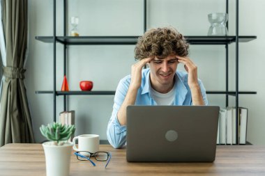 Kafkasyalı stres işadamı evden çalışırken bilgisayarda yazı yazıyor. Depresyondaki çekici serbest çalışan adam masaya oturur, dizüstü bilgisayarı kullanır, online plan projesini evdeki oturma odasında yapar..