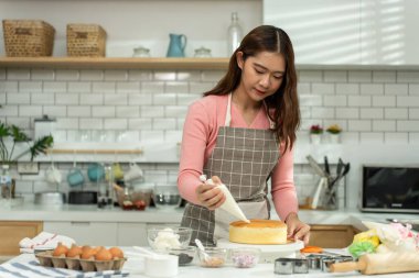 Asyalı güzel bir kadın evdeki mutfak odasında pasta ve fırın yapıyor. Önlük giyen çekici genç kız, mutlu ol ve rahatla. Keyfine bak. Boş vakitlerini geçir..