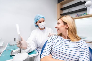 Kadın diş hekimi, diş sağlığı kliniğindeki beyaz dişli kızı muayene ediyor. Diş hekimliği koltuğunda yatan çekici kadın hastanede muayene sırasında doktordan diş tedavisi görüyor.