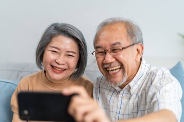 Asya 'daki son sınıf öğrencileri, aileleriyle evlerinde video görüşmesi yapıyor. Çekici yaşlı yetişkin erkek ve kadın ebeveyn koltukta oturuyor cep telefonu kullanarak evdeki akrabalarıyla sanal iletişim kuruyorlar.