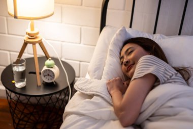 Asian beautiful woman lying down on bed in bedroom, dreaming at night. Attractive young female in pajamas sleeping alone on comfortable pillow and cozy blanket in dark room for health care at home.