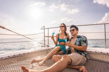 Yatta parti yaparken şampanya içen Asyalı güzel çift. Çekici bir erkek ve kadın birlikte takılıyor, yıl dönümü balayı gezisini kutlarken katamaran teknesi yaz günbatımında yelken açıyor..