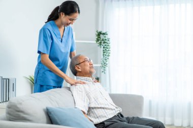 Huzurevinde yaşlı bir adamla ilgilenen Asyalı kadın hemşire. Genç, hasta bakıcı doktor yaşlı, mutlu, engelli büyükbaba hastasına masaj yapıyor. Sağlık sigortası konsepti.