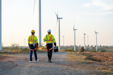 Rüzgâr türbinleri alanında yürüyen çeşitli etnik kökenli erkek teknisyenler. Yenilik mühendisi güvenlik donanımı giyen adamlar, çevresel yenilenebilir temiz enerji geliştirmek için yel değirmeni çiftliğinde çalışıyorlar.