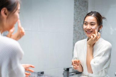 Asyalı güzel kadın yüz bakımı için yumuşak ve cilt bakımı yapıyor. Çekici kadın dokunuşları ve gençleşme için krem sürme duştan sonra nazikçe. Güzellik, cilt bakımı ve sağlık.