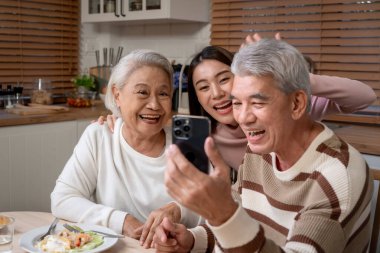 Asyalı bir aile akşamları evde yemek yerken selfie çekiyor. Büyükbaba ve kız telefonda fotoğraf çekiyorlar. Yemek yerken hafta sonlarını evde birlikte geçiriyorlar..