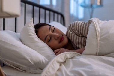 Asian beautiful woman lying down on bed in bedroom, dreaming at night. Attractive young female in pajamas sleeping alone on comfortable pillow and cozy blanket in dark room for health care at home.