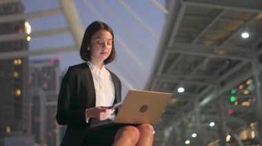 Beyaz tenli güzel iş kadını, bilgisayarda çalışıyor ve daktilo kullanıyor. Acil işi tamamlamak için geceleri dışarıda oturuyor. Akıllı telefondan konuşan genç kız çalışanlar, modern ağ teknolojisinin tadını çıkarın..