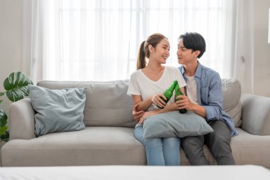 Asyalı genç çift boş zamanlarını birlikte oturma odasında geçiriyorlar. Çekici yeni evli erkek ve kadın mutlu ve rahat hissediyorlar, evde bir şişe bira içiyorlar. Evde etkinlik ilişkisi.