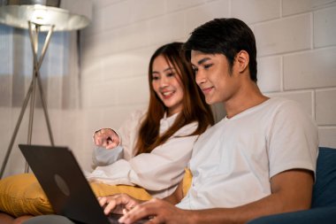 Asyalı genç adam geceleri karısıyla birlikte evde dizüstü bilgisayar kullanıyor. Pijamalı çekici bir eş kocasını beklerken evde yatmadan önce internette iletişim kuran bir defter kullanıyor..