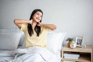 Asyalı genç ve güzel bir kadın sabah yataktan kalkıyor. Pijamalı çekici kız mutlu ve rahat hissediyor, uyanıyor ve hafta sonu yatak odasında vücudunu esnetiyor..