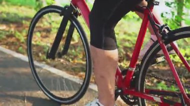 Genç aktif adamın bacakları yeşil parktaki sağlık için yürüyüş bisikletine binmeye başlıyor.