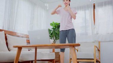 Antrenman yapan Asyalı genç kadın spor yapıyor. Canlı spor programı veya evdeki dizüstü bilgisayarda video öğretim programı izliyorlar..