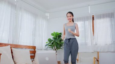 Antrenman yapan genç Asyalı kadın, evde dizüstü bilgisayarda eğitmeni takip ediyor.