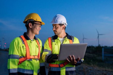 Rüzgar türbinleri alanında çalışan çeşitli etnik kökenli erkek teknisyenler. Yenilik mühendisi erkekler, yel değirmeni enerji çiftliğinde çevresel yenilenebilir temiz enerji geliştirmek için dizüstü bilgisayar kullanırlar..