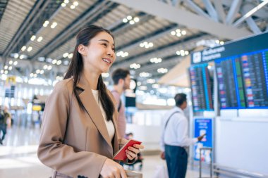 Asyalı genç bir kadın yolcu havaalanından geçiş kartını kontrol ediyor. Çekici güzel bayan turist arkadaşları tatil gezisi için uçakla yurtdışına gitmekten mutlu ve heyecanlı hissediyorlar..