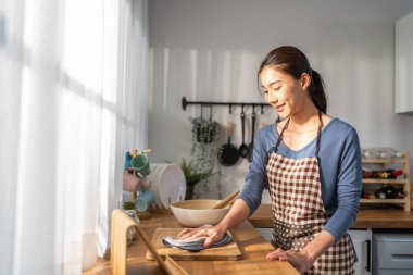 Asyalı güzel temizlikçi kadın evdeki mutfağı temizliyor. Güzel bayan ev hanımı temizlikçi mutlu ve temizlik işleri için kirli yemek masasını siliyor.