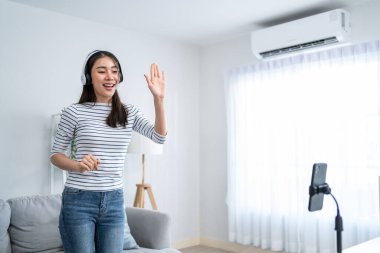 Asyalı çekici kadın evdeki oturma odasında müzikle dans etmekten hoşlanıyor. Güzel bir kadın cep telefonuyla meydan okuma videosu kaydediyor. Sanal bir klipte şarkı söylüyor, hafta sonu evde aktivitelerin keyfini çıkarıyor..